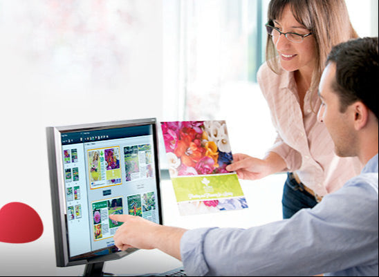 Two people looking at a computer screen with a colorful brochure and Fiery Command Workstation